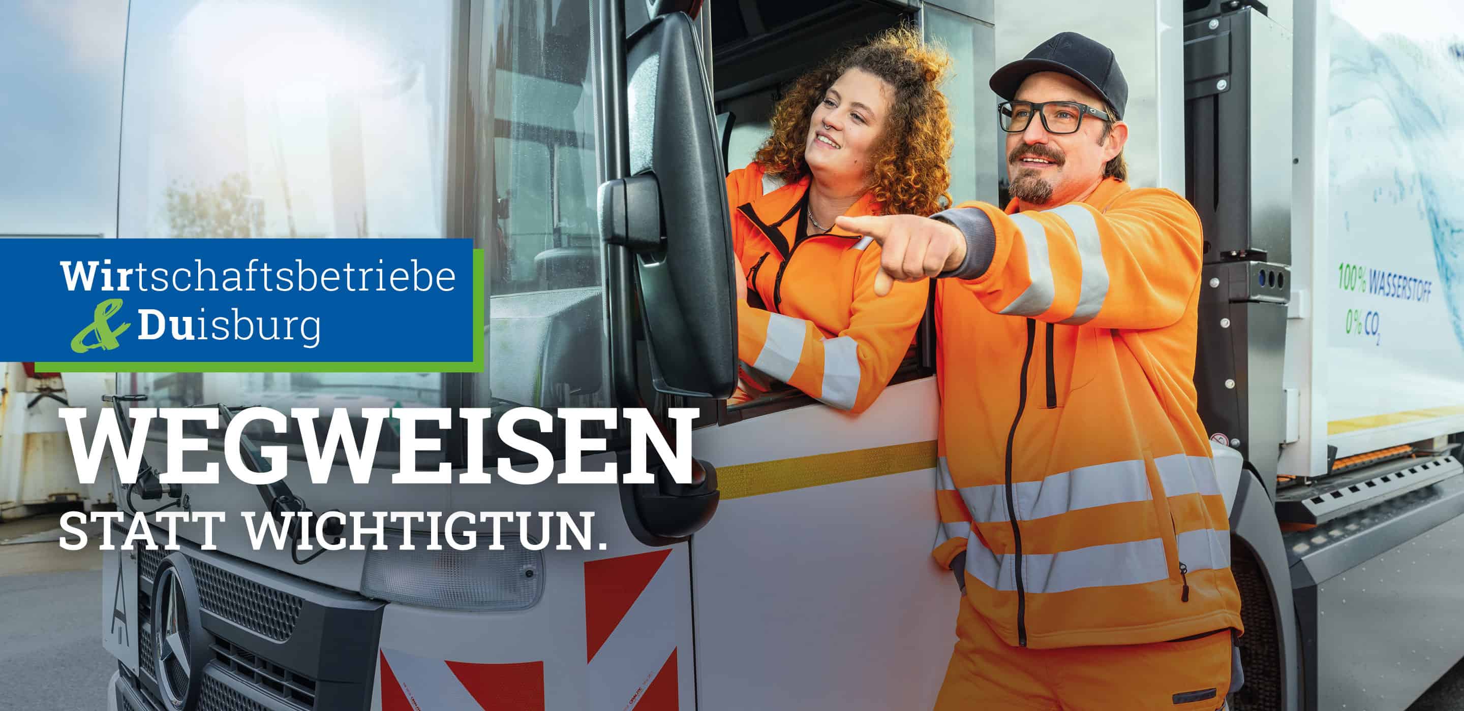 Zwei Mitarbeitende der Wirtschaftsbetriebe Duisburg in orangefarbener Arbeitskleidung an einem Fahrzeug mit dem Slogan „Wegweisen statt wichtigtun.“